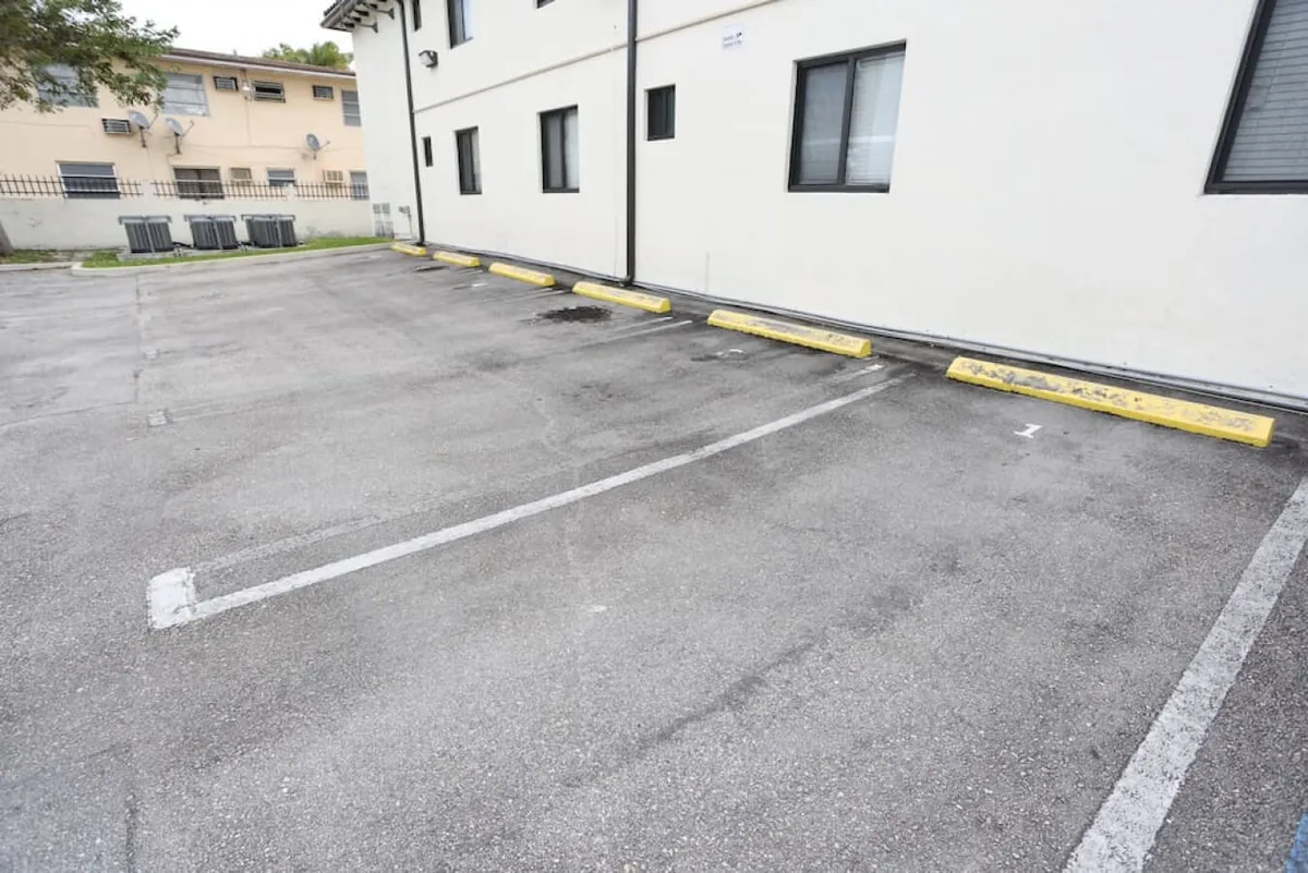This image displays a clean, empty parking space marked with the number 1, bordered by yellow parking bumpers and adjacent to a white building wall with several windows. The scene is practical and neutral, emphasizing the ease and convenience of on-site parking for guests.